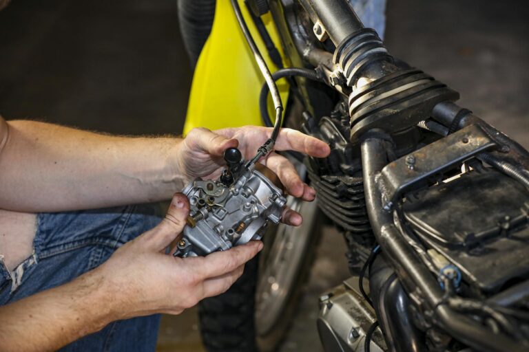Close-up of a mechanic's hands fixing a motorcycle carburetor.