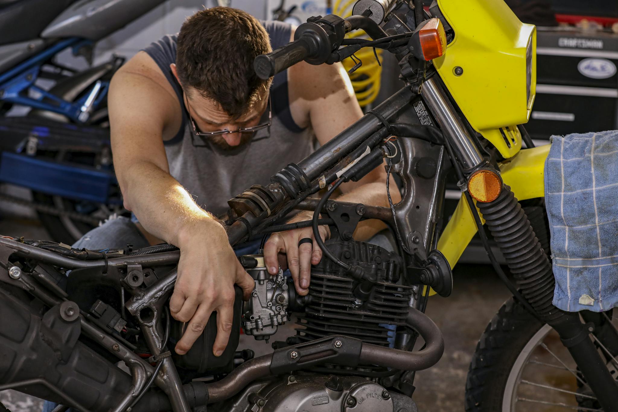 Mechanic intricately repairing motorcycle engine in a garage environment.